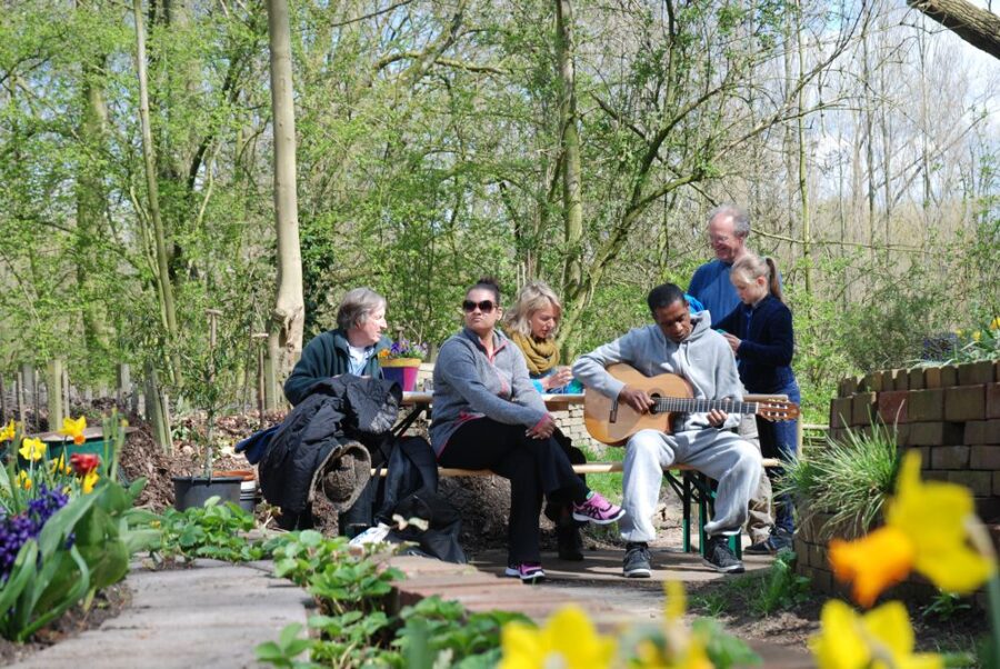 People gathered on a bench in Oost Indisch Groen, Amsterdam, enjoying a lively music session in the community garden.