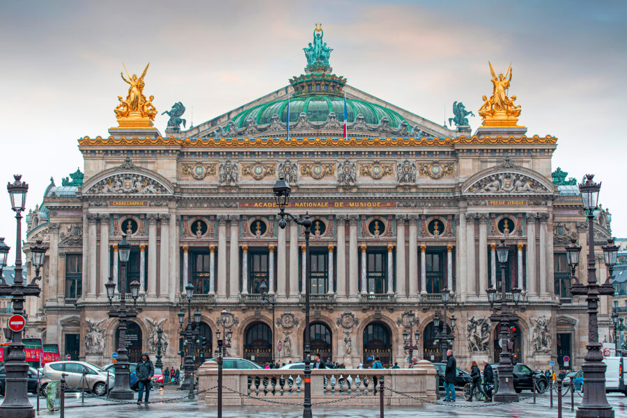 Palais Garnier's stunning facade in Paris, captured on a rainy spring day, with droplets on the ground and cloudy skies.