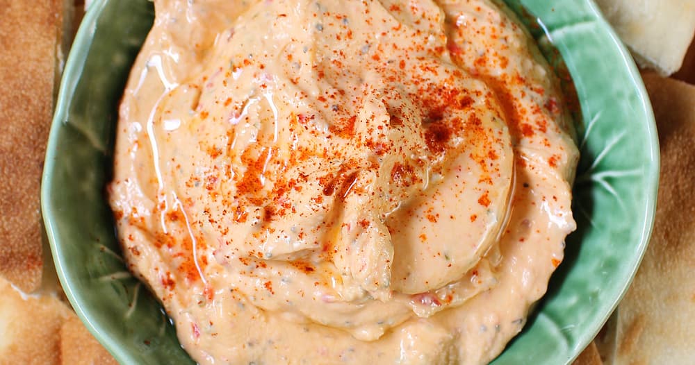 Creamy orange Mediterranean dip in a green bowl with paprika, bread, and crackers.