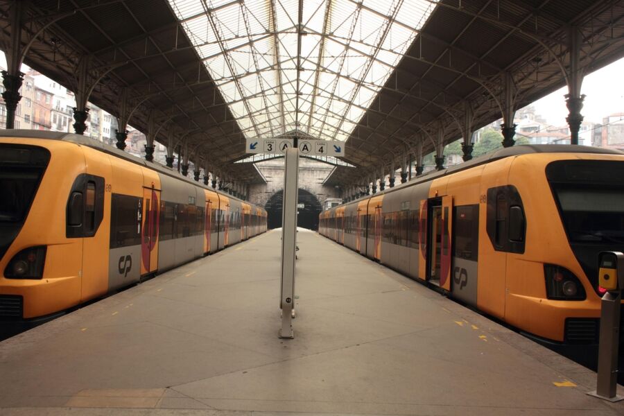 Modern train station with orange CP trains, glass roof, platform signage, and tunnel.