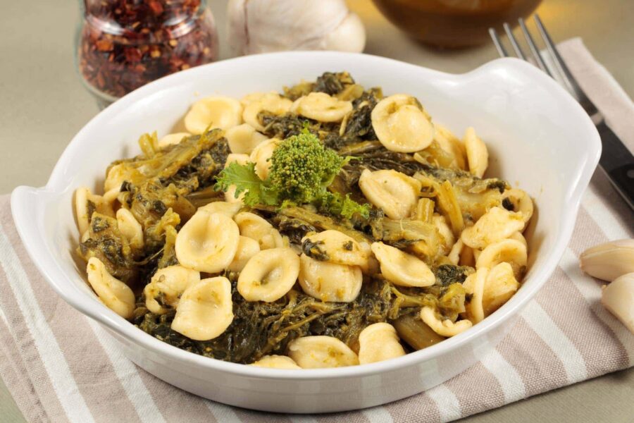 Orecchiette pasta with sautéed greens in a white bowl, Italian cuisine.