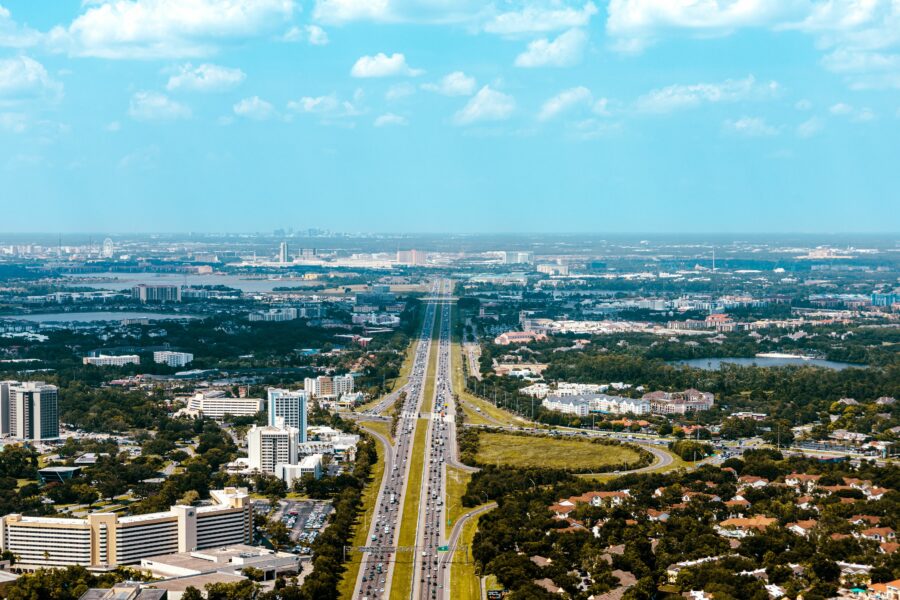 Aerial view of a busy highway with the Orlando city skyline in the background under a clear blue sky.