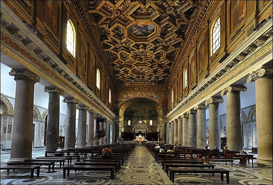 Ornate basilica nave with gilded coffered ceiling, marble floor, columned aisles, and distant altar.