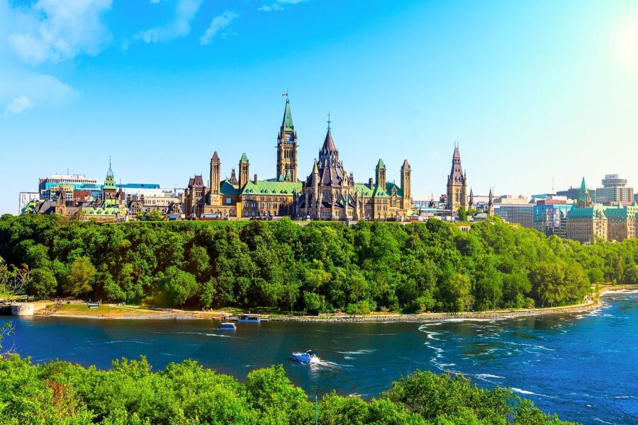 Parliament Hill in Ottawa, Canada, overlooking the Ottawa River with lush greenery and Gothic architecture.