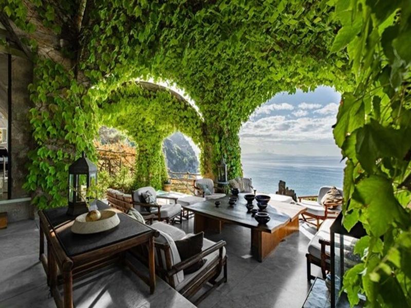 Outdoor living space with modern design, lush greenery, sea view, and elegant furnishings.