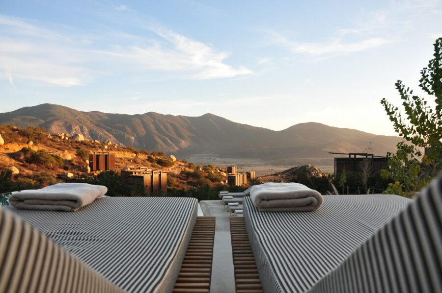 Sunset mountain view with loungers, wooden deck, and modern structures in serene landscape.