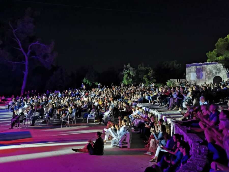 Hvar Summer Festival night concert audience in stone amphitheater under colorful lights.