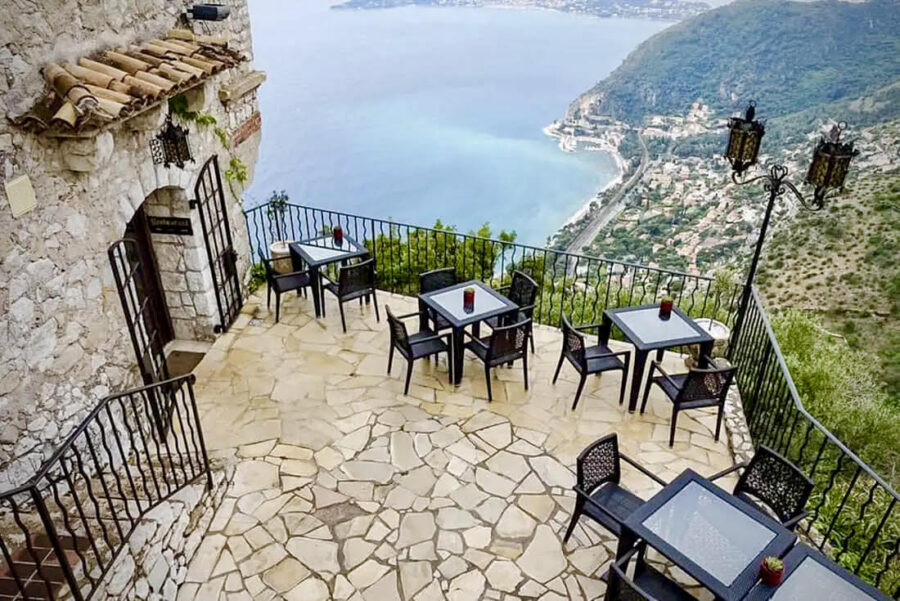 Terrace with ocean-view dining, rustic stone building, and scenic coastal landscape.