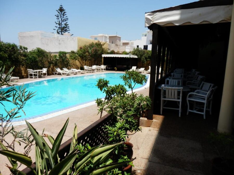 Sunny riad hotel pool with turquoise water, loungers, shaded patio, lush garden walls.