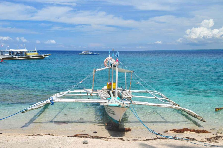 Outrigger boat on sandy beach at Apo Island with turquoise sea and clear tropical sky.