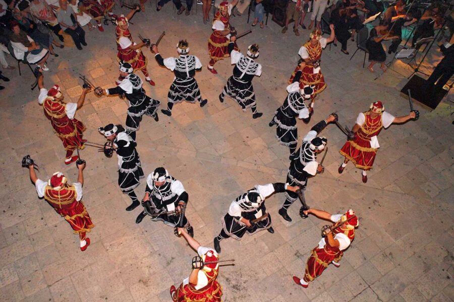 Moreška sword dance performers in colorful historical costumes, overhead courtyard view.
