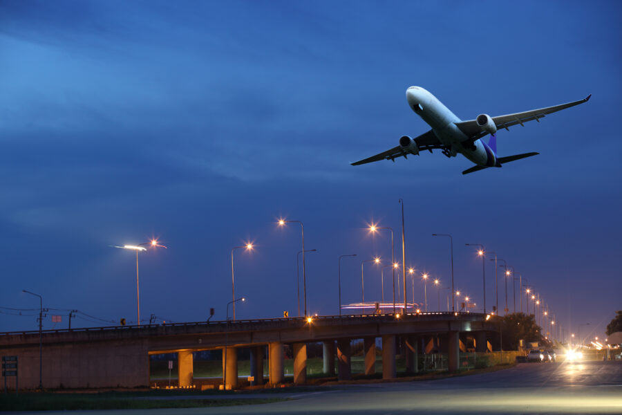 White aircraft takes off from the airport runway at night, illuminated by runway lights against a dark sky