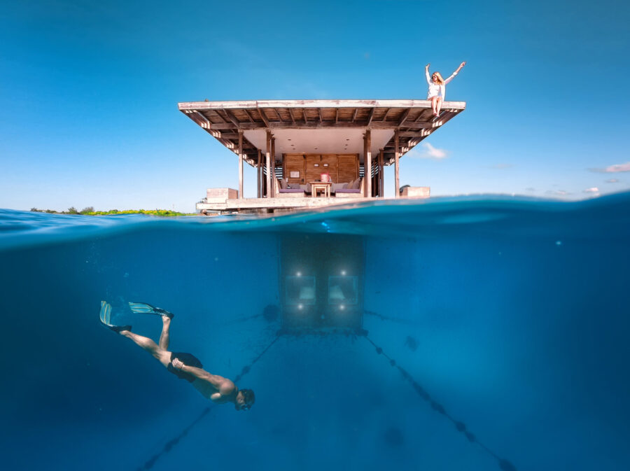 Luxury floating sea villa with underwater room, snorkeler, and woman enjoying tropical ocean vacation.