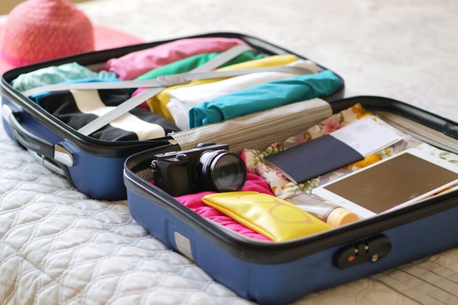 Packed suitcase for tropical vacation with clothing, camera, passport, and beach hat.