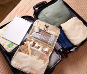 Open suitcase with neatly packed clothes, a green sweater, beige shirt, jeans, a toiletry bag, notebook, and a map. It conveys readiness for travel.