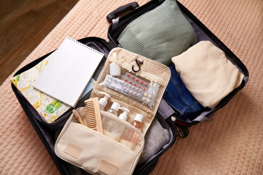 Open suitcase with neatly packed clothes, a green sweater, beige shirt, jeans, a toiletry bag, notebook, and a map. It conveys readiness for travel.