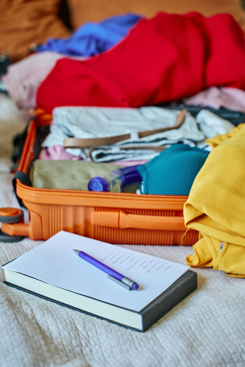 Handwritten checklist and pen on clothes inside a suitcase, illustrating travel preparation for a holiday or vacation