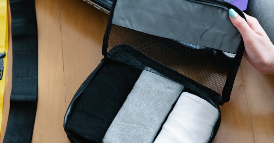 Small travel packing cube with rolled shirts organized inside on a wooden surface.