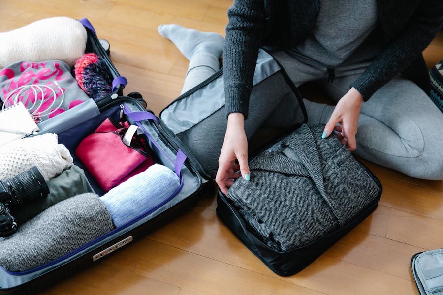 Woman packing organized suitcase with packing cubes and clothes on wooden floor for travel.