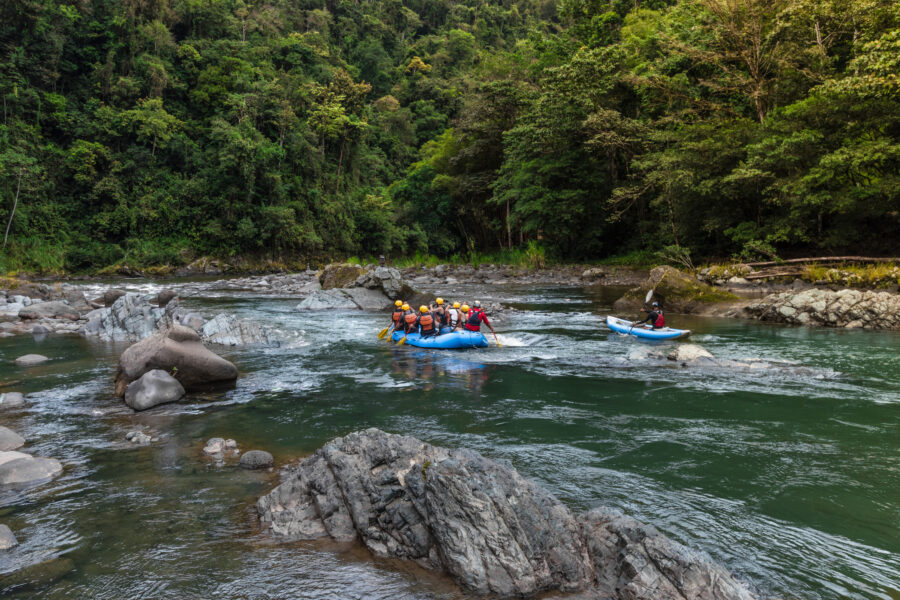 Tourists navigate a raft and kayak on the Pacuare River, immersed in the vibrant jungle scenery of Costa Rica