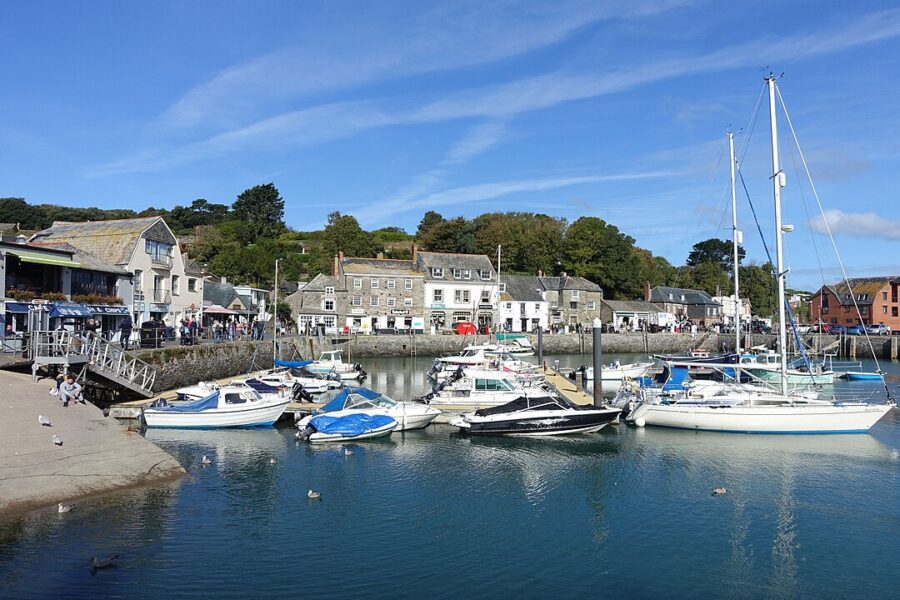 Several boats are moored at a picturesque harbor in Padstow, Cornwall, England, surrounded by charming buildings.
