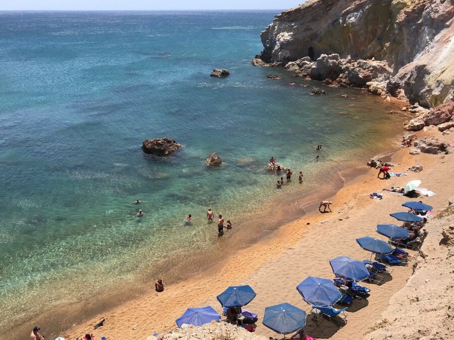 Crowded beach in Paleochori, Greece, filled with people relaxing under colorful umbrellas.