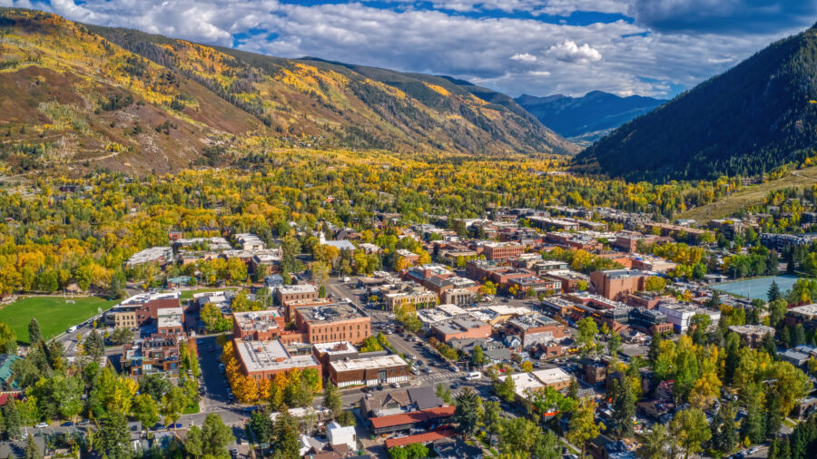 Aerial view of Aspen, Colorado, showcasing vibrant autumn foliage and the surrounding mountains under a clear blue sky