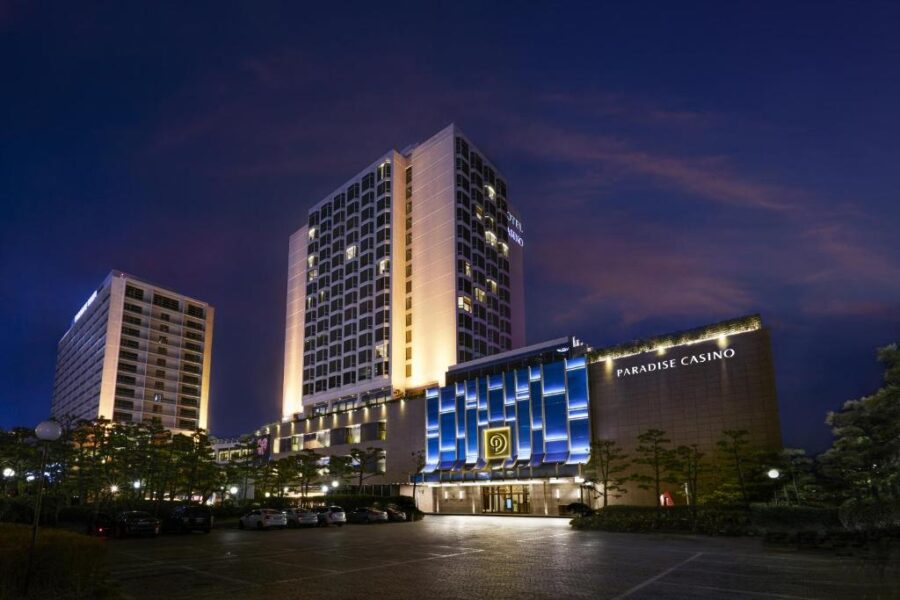 Night view of Paradise Casino hotel in Busan with illuminated towers, luxury entrance, and parking.