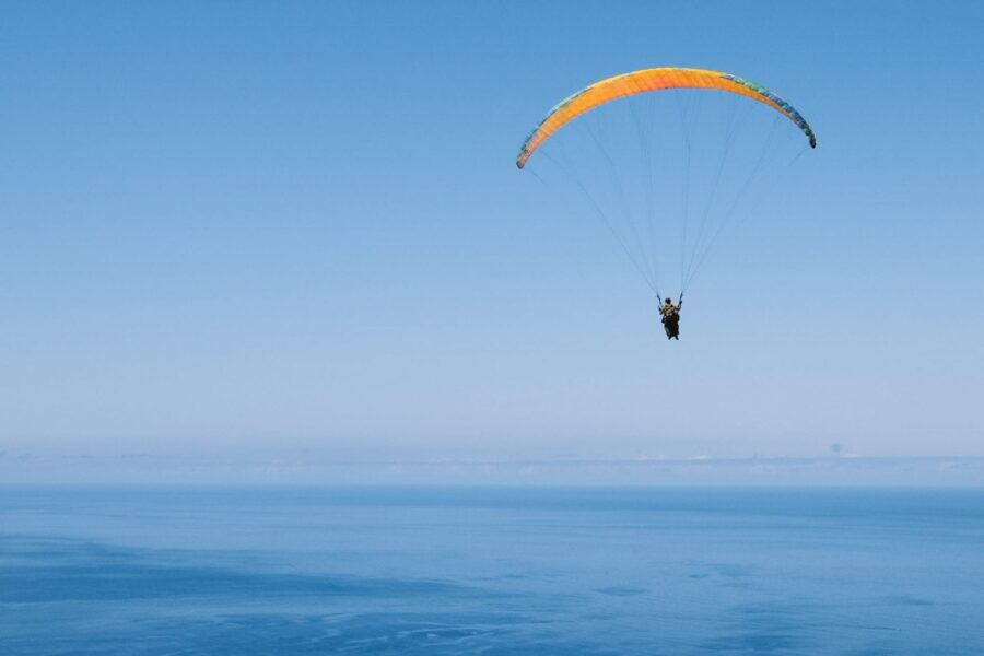 Paraglider soaring over Funchal ocean with blue sky and coastal horizon.