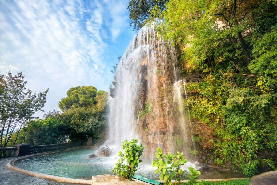 Waterfall cascading down rocks in Parc de la Colline du Chateau, surrounded by lush greenery in Nice, Cote d'Azur, France