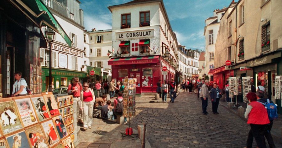 Charming Paris street scene with Le Consulat café, art displays, and lively tourists in Montmartre.
