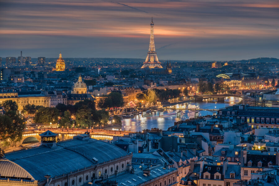 Panoramic view of Paris at night, showcasing illuminated landmarks like the Eiffel Tower and the Seine River.