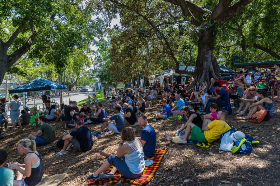 Crowd enjoying live music and food under trees at Davies Park market festival.