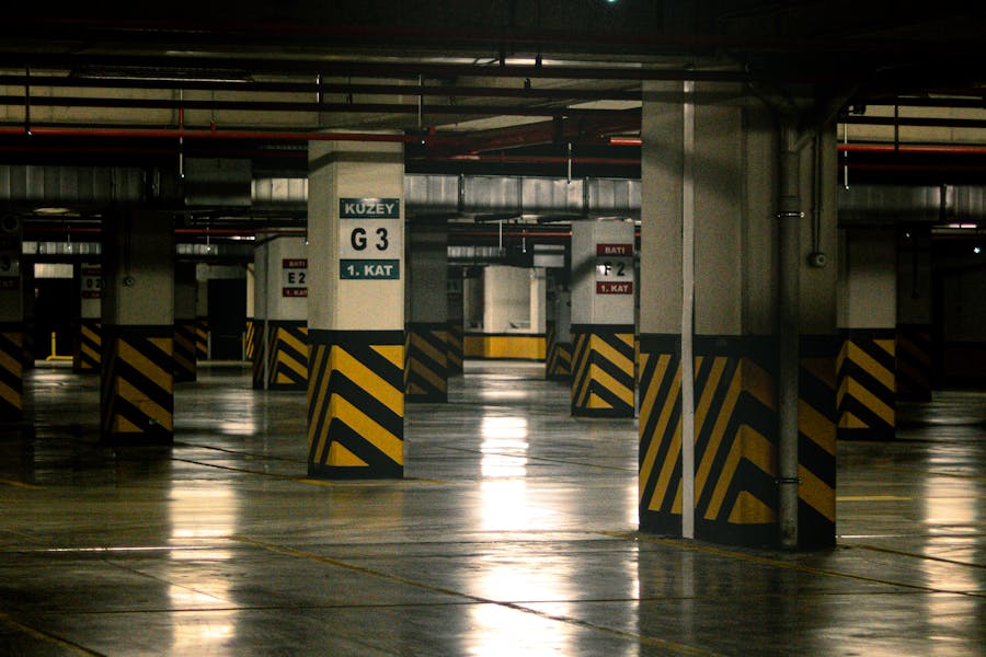 Empty underground parking garage with concrete columns, yellow-black safety stripes, and polished reflective floor.