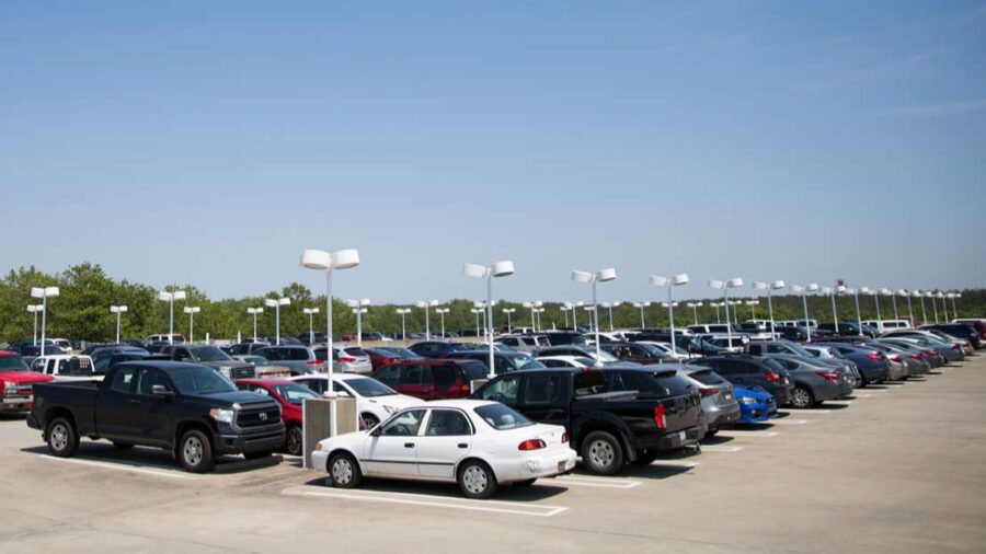 Full daytime parking lot with rows of cars and lamp posts, ideal for parking reservations.