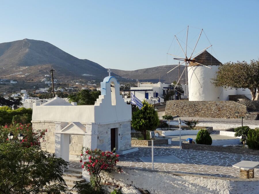 In Paros, Greece, a picturesque windmill and a white church are seen in a quaint small town setting.