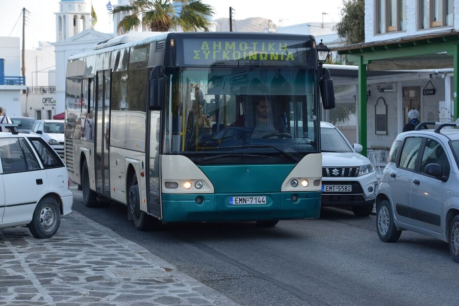 Bus traveling along a street in Paros, Greece, with local architecture in the background.