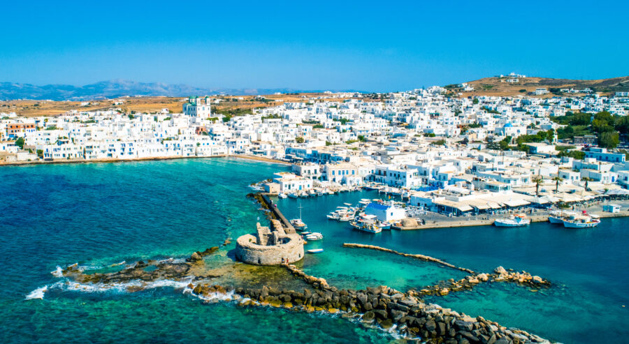 Aerial view of ancient Venetian castle ruins in Naoussa harbor, Paros island, Greece, surrounded by blue waters.