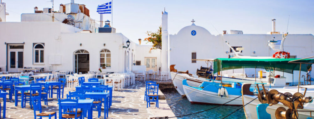 Scenic view of Naousa village in Paros, Greece, featuring whitewashed buildings and vibrant blue sea under a clear sky.