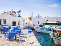 Scenic view of Naousa village in Paros, Greece, featuring whitewashed buildings and vibrant blue sea under a clear sky.