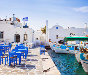 Scenic view of Naousa village in Paros, Greece, featuring whitewashed buildings and vibrant blue sea under a clear sky.
