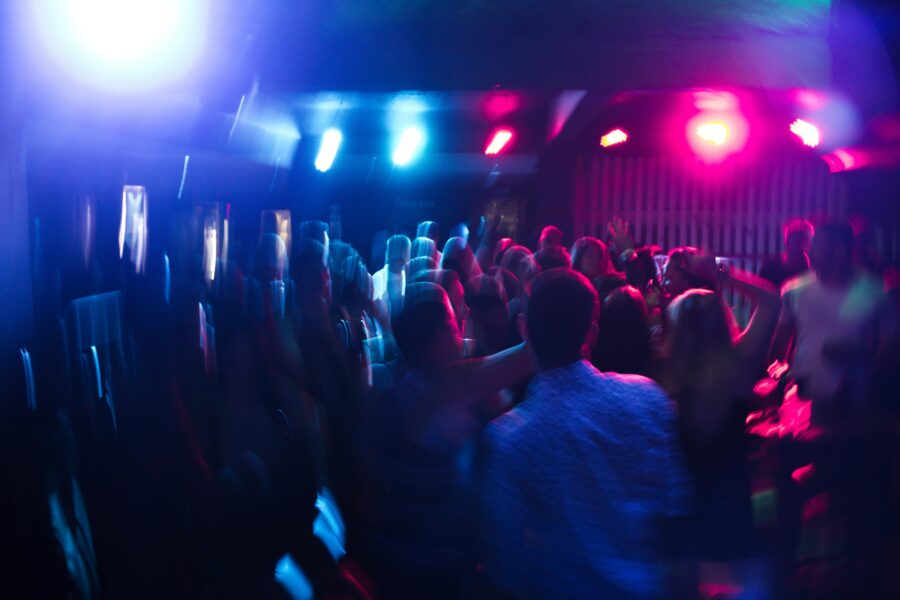 Vibrant nightlife scene with people dancing under colorful lights at a lively club party.