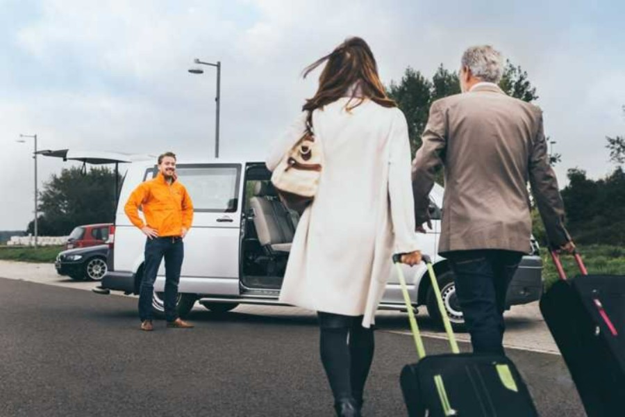 Passengers boarding shuttle van with luggage at roadside pickup.