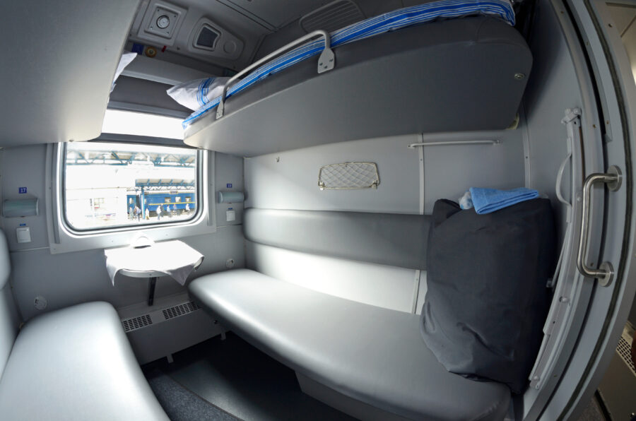 Cozy First Class sleeping carriage compartment featuring a made bed and neatly arranged linen packages for passengers.