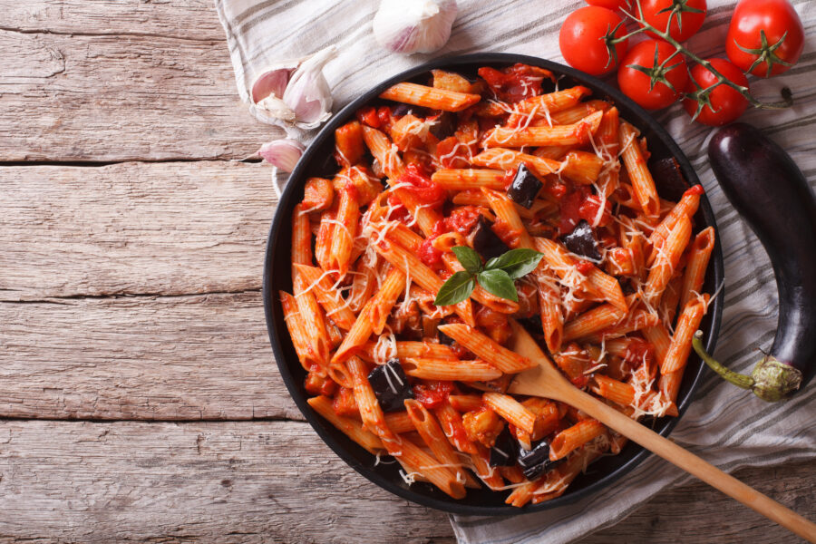 Close-up of Pasta alla Norma with eggplant, tomatoes, and basil, viewed from above, showcasing vibrant colors and textures
