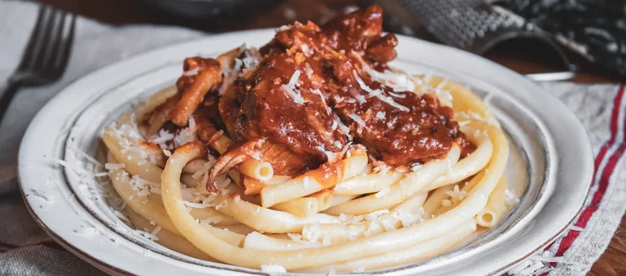 Pasta ragu with shredded meat and Parmesan on a rustic white plate.