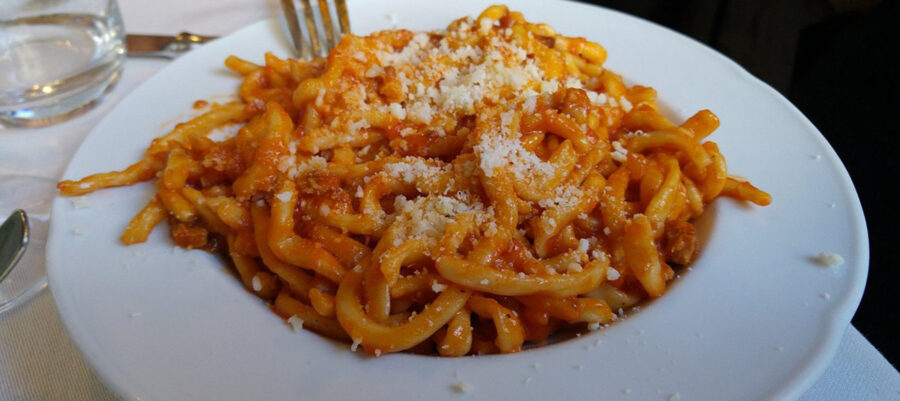 Close-up of umbrichelli pasta in tomato sauce with cheese, in a rustic, Italian setting.