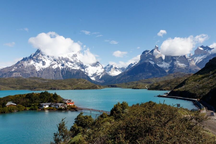 Beautiful Patagonia landscape with mountains, turquoise lake, wooden bridge, and quaint building.