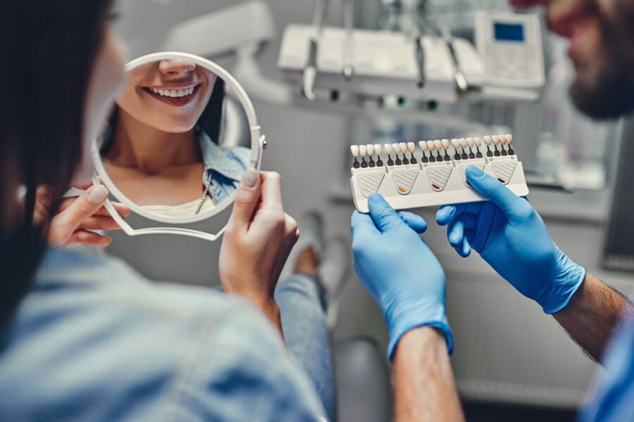 Smiling dental patient admires new teeth with dentist using shade guide for color match.