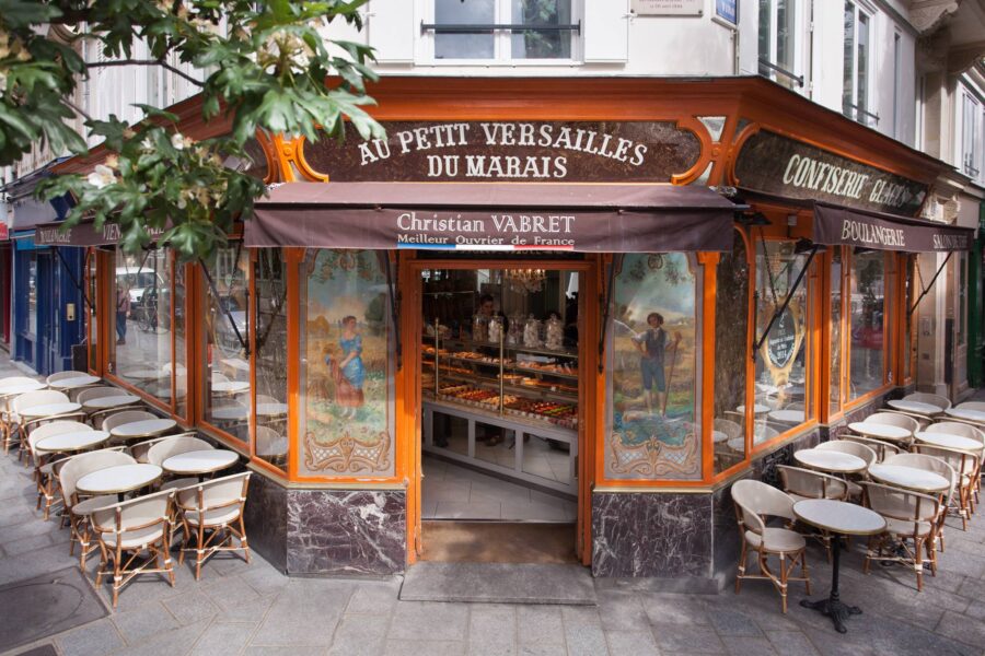 Parisian patisserie-cafe terrace with pastries, outdoor bistro tables and wicker chairs.